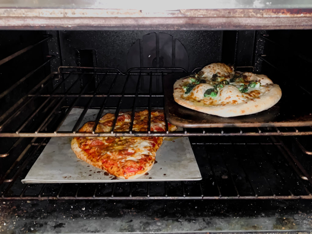 Two pizzas ready to come out of the oven, both made using the Trapper's Pizza Pub Make-Your-Own Pizza Kits. 