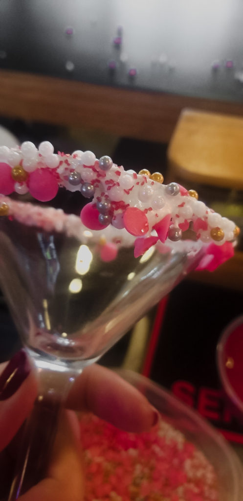 Pink, white, purple, and gold sprinkles adorn the rim of a martini glass for Trapper's Pizza Pub's extra special Cupid's Arrow cocktail. 